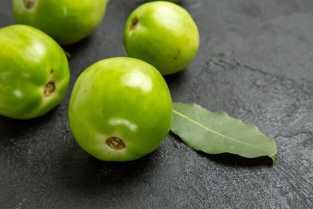 Vista inferior de tomates verdes e folha de louro em fundo escuro