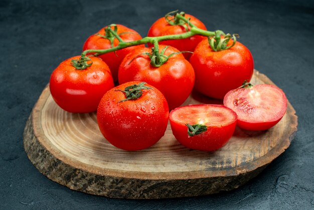 Vista inferior de tomates vermelhos em uma placa de madeira na mesa escura