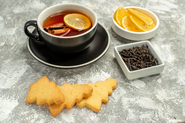 Vista inferior de uma tigela de chá com limão e biscoitos em pau de canela com chocolate na superfície cinza