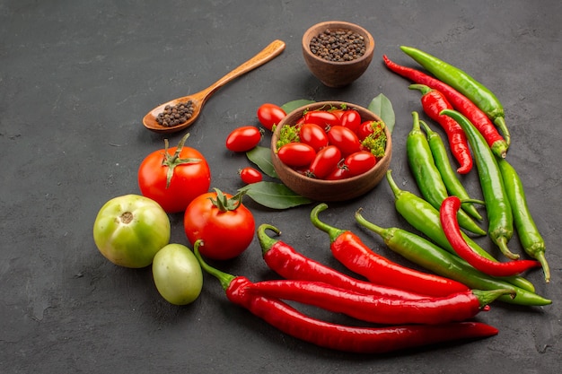 Vista inferior de uma tigela de tomates cereja quentes pimentões vermelhos e verdes e tomates pimenta preta em uma colher de madeira uma tigela de pimenta preta no fundo preto