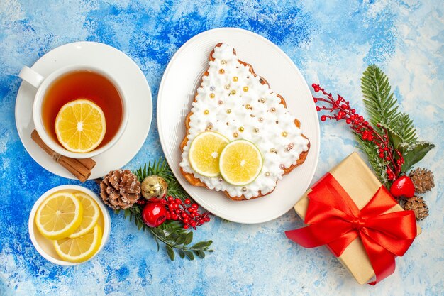 Vista inferior de uma xícara de chá, bolo de fatias de limão no prato, presente de Natal na mesa azul