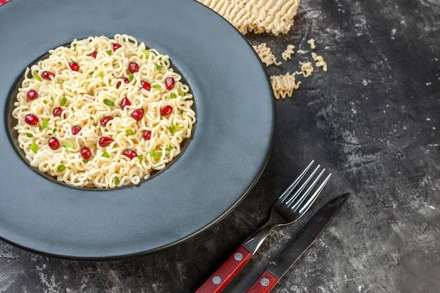 Foto grátis vista inferior do macarrão ramen em prato redondo escuro garfo de toalha de mesa quadriculada vermelha e branca e faca macarrão ramen cru na mesa escura