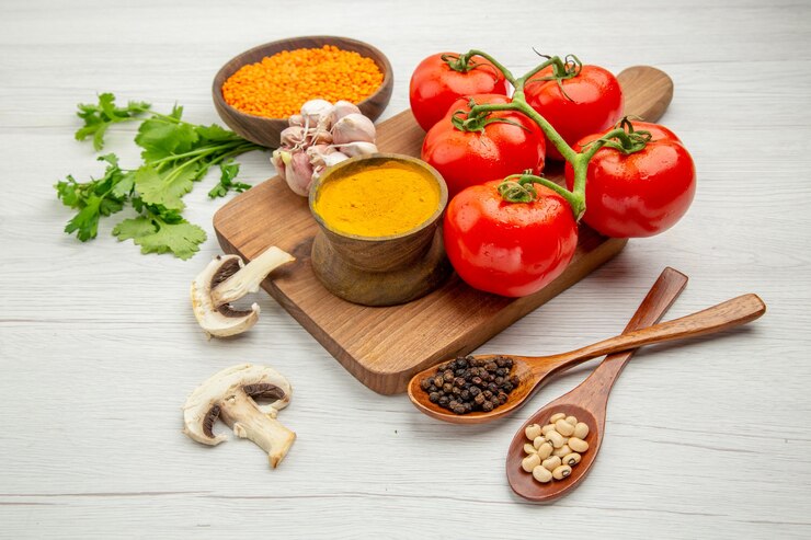 Foto grátis vista inferior do ramo de tomate fresco alho açafrão na tábua de cortar cogumelos pimenta preta e feijão em colheres de madeira na mesa cinza