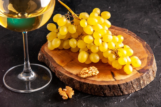 Vista inferior do vinho branco em vidro de uvas amarelas na placa de madeira na mesa escura
