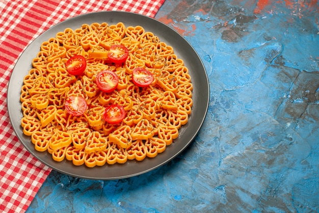 Vista inferior dos corações de massa italiana cortam tomates cereja em uma placa oval na mesa quadriculada branca vermelha