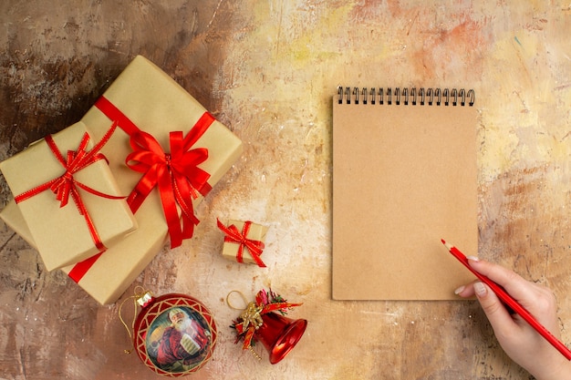 Vista inferior dos presentes de natal em fita de papel pardo, brinquedo de árvore de natal no jornal em fundo escuro