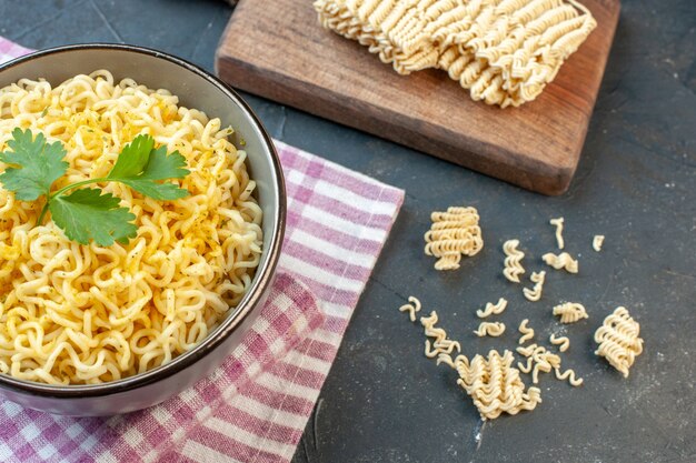 Vista inferior macarrão ramen asiático em uma tigela na toalha de mesa quadriculada rosa branca macarrão ramen cru na tábua de cortar na mesa escura