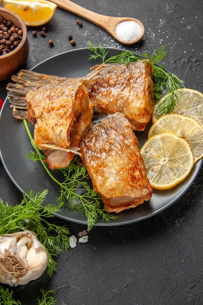 Vista inferior peixe frito pimenta preta em uma tigela menta rodelas de limão colher de madeira na mesa preta