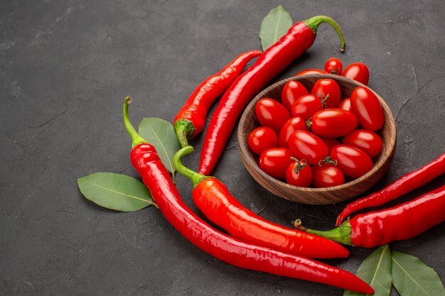 Vista inferior semicírculo com pimentas vermelhas e folhas de louro e uma tigela de tomates cereja no lado direito da mesa preta