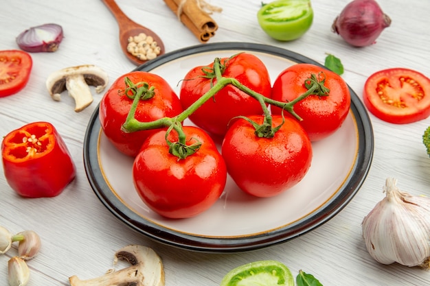 Vista inferior tomate vermelho no prato branco alho cogumelo anis ervilhas pretas na colher de pau canela em pau cebola na mesa cinza