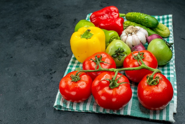 Vista inferior vegetais alho pepinos tomate ramo tomates verdes pimentões na toalha de mesa verde na mesa preta com espaço livre