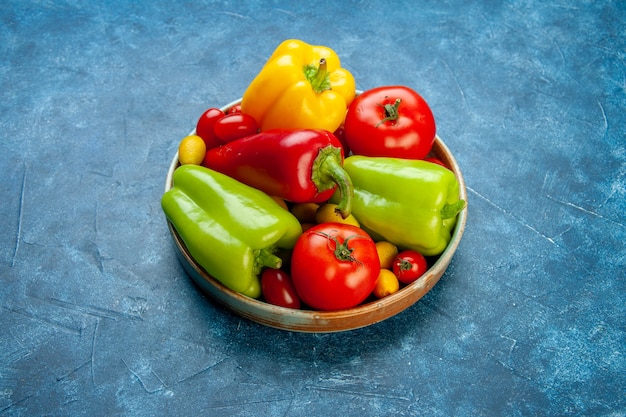 Vista inferior vegetais tomates cereja cores diferentes pimentões tomates cumcuat em uma bandeja de madeira na mesa azul