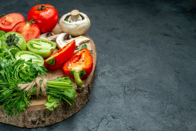 Vista inferior vegetais tomates pimentões verdes cogumelo na placa de madeira no espaço livre da mesa preta