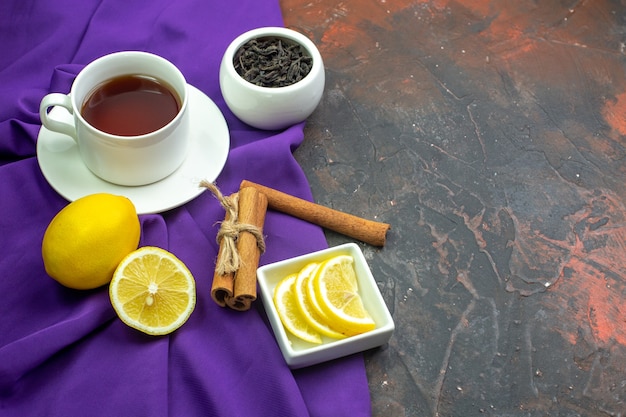 Foto grátis vista inferior xícara de chá fatias de limão em uma tigela canela paus de chá em uma tigela na toalha de mesa roxa na mesa vermelha escura