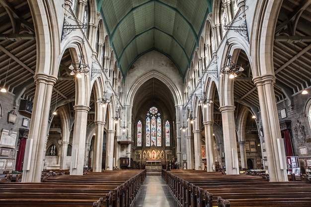 Vista interna de uma igreja com ícones religiosos nas janelas e arcos de pedra