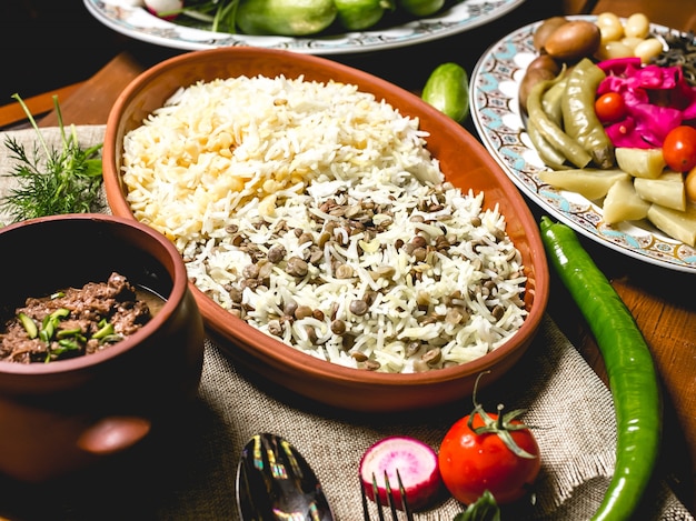 Vista lateral arroz cozido em um prato com carne em uma panela e legumes salgados