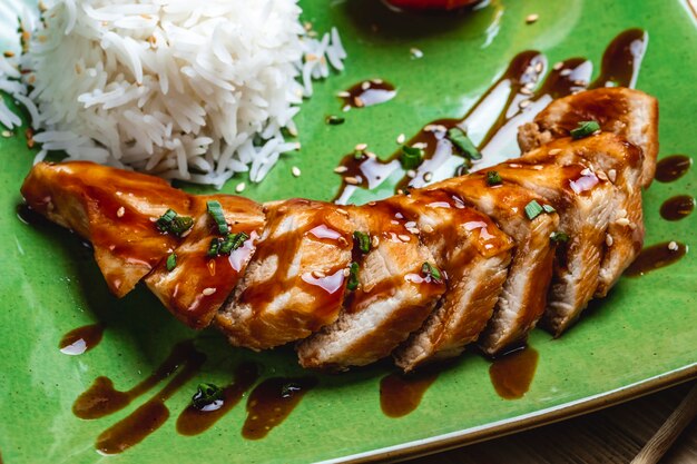 Vista lateral assado peito de frango com molho de cebola primavera sementes de gergelim e arroz em um prato