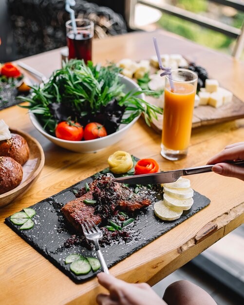 Vista lateral bife grelhado carne vermelha tomate pepino e limão em uma placa