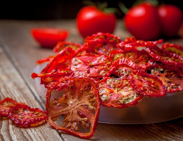 Vista lateral close-up tomates secos no prato e tomates frescos na mesa de madeira