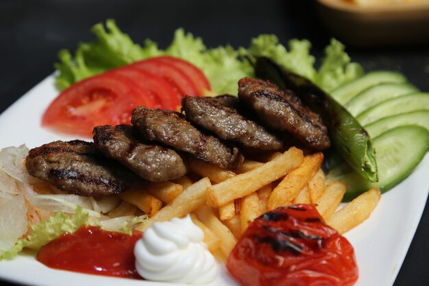 Vista lateral costeleta de carne frita com batatas fritas tomates pimentas pepinos e ketchup com maionese em um prato