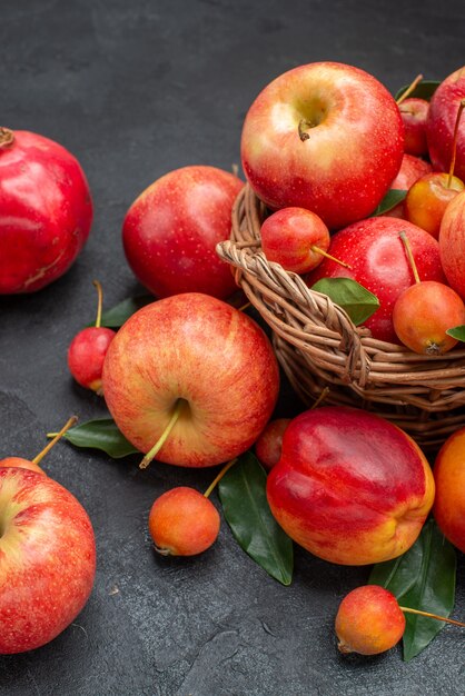 Vista lateral da cesta de frutas com maçãs, cerejas, folhas, nectarina, romãs