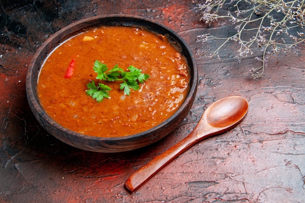 Vista lateral da clássica sopa de tomate em uma tigela marrom e uma colher na mesa de cores diferentes