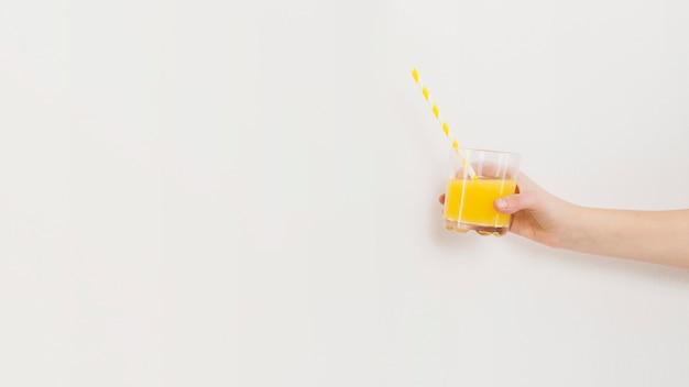 Vista lateral da mão segurando o copo com suco e palha com espaço de cópia