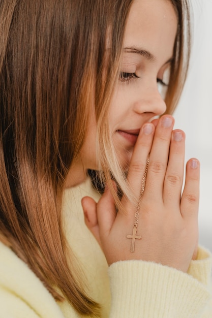 Vista lateral da menina rezando com colar de cruz