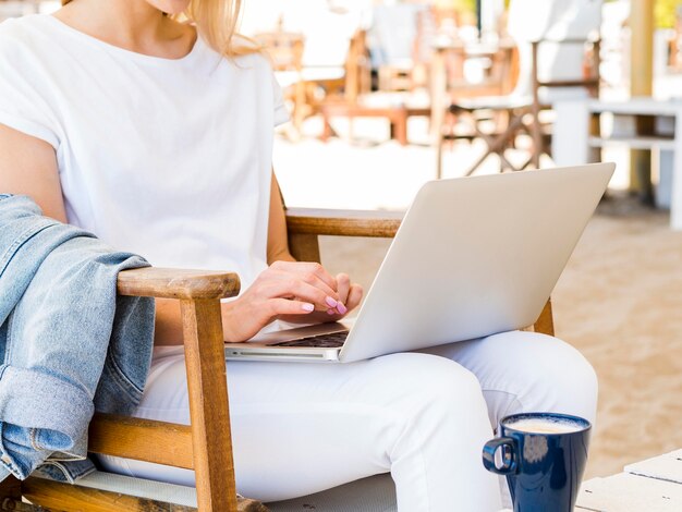 Vista lateral da mulher ao ar livre na cadeira trabalhando no laptop