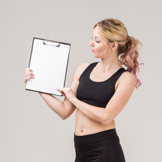 Vista lateral da mulher atlética segurando um bloco de notas em branco