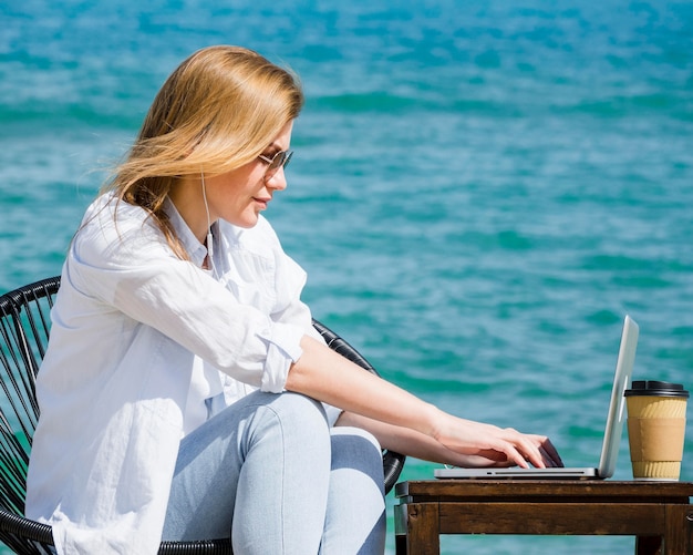 Vista lateral da mulher na praia trabalhando no laptop