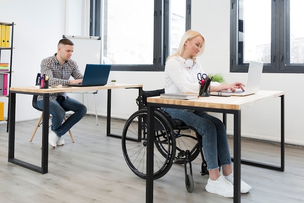 Vista lateral da mulher no trabalho de cadeira de rodas formar sua mesa