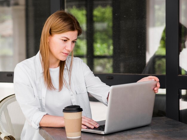 Vista lateral da mulher que trabalha ao ar livre enquanto tomando café