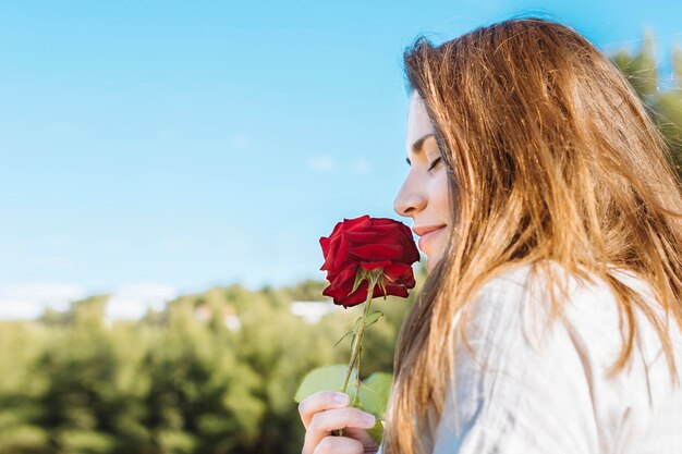Vista lateral da mulher segurando e cheirando a rosa