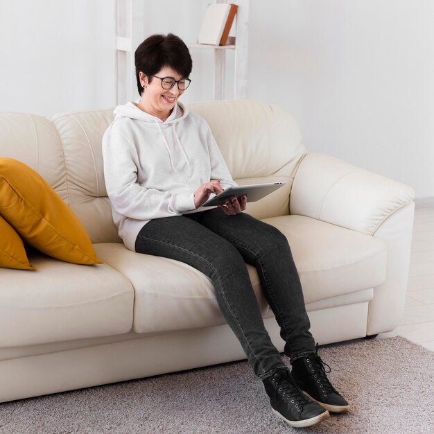 Vista lateral da mulher sentada no sofá com tablet
