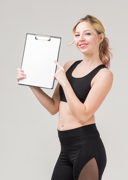 Vista lateral da mulher sorridente em athleisure segurando o bloco de notas