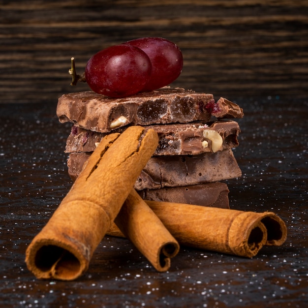 Vista lateral da pilha de leite e chocolate escuro com frutas e bagas de nozes e paus de canela em fundo escuro