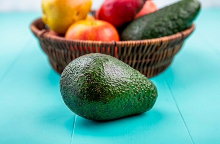 Foto grátis vista lateral de abacate com um balde de frutas como pêra de romã na superfície azul