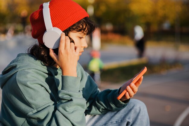 Vista lateral de adolescente ouvindo música em fones de ouvido enquanto usa o smartphone