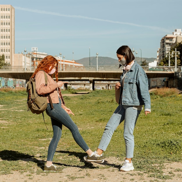 Vista lateral de amigas com máscaras ao ar livre tocando os tornozelos