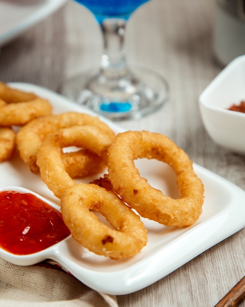 Vista lateral de anéis de cebola frita com ketchup em uma mesa