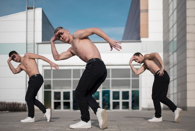 Vista lateral de artistas de hip hop masculino sem camisa dançando lá fora