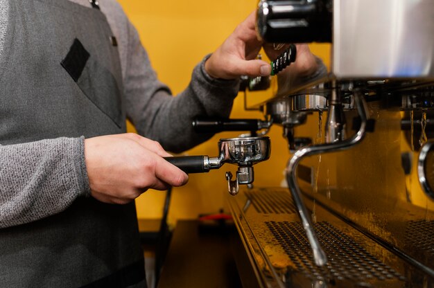 Vista lateral de barista masculino com avental usando máquina de café profissional