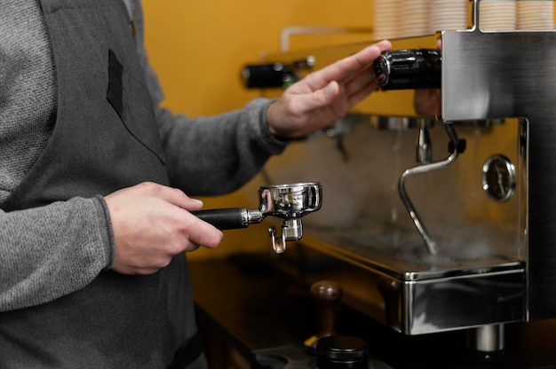 Vista lateral de barista masculino com avental usando máquina de café profissional