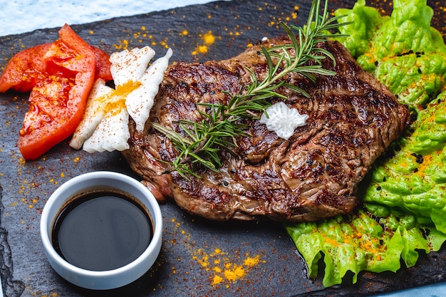 Vista lateral de bife grelhado de carne vermelha com alecrim tomate alface e molho de romã em uma bandeja