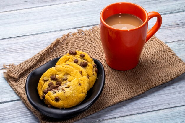 Vista lateral de biscoitos de aveia com pepitas de chocolate e uma caneca com bebida de cacau em um de madeira