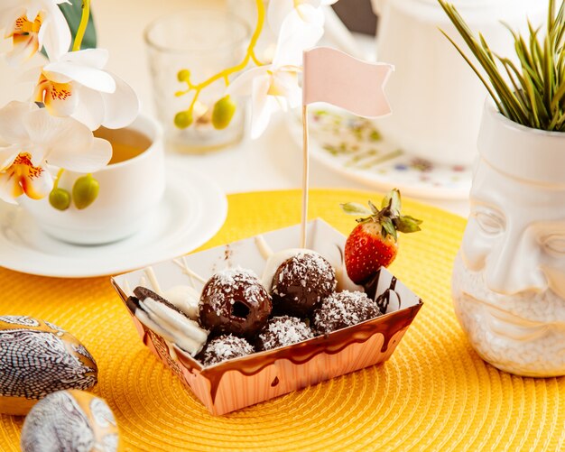 Vista lateral de bolas de chocolate com granulado de coco e morango em um saco de papelão