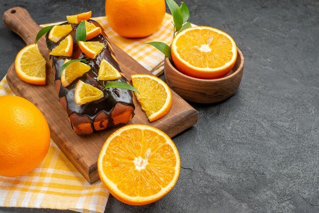 Vista lateral de bolos moles inteiros e laranjas cortadas com folhas na mesa escura