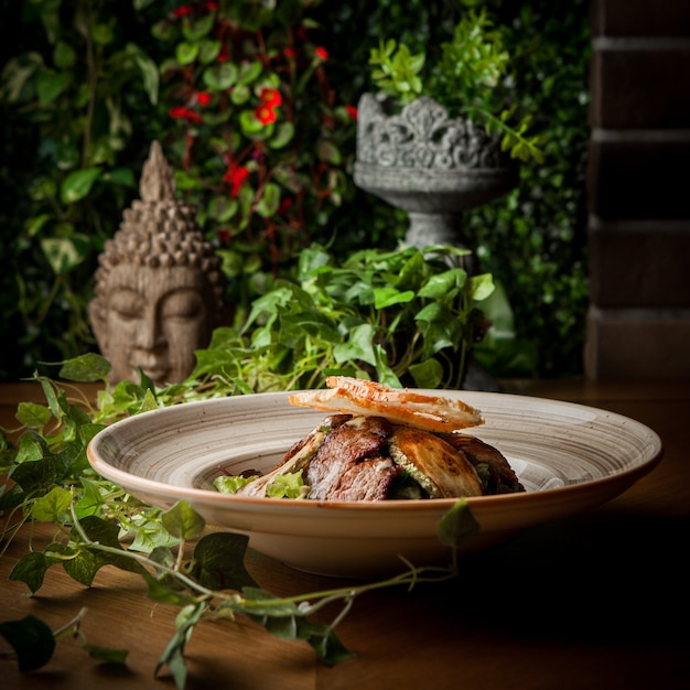 Foto grátis vista lateral de carne frita com abobrinha frita e ramo de uva e cabeça de estátua em prato redondo