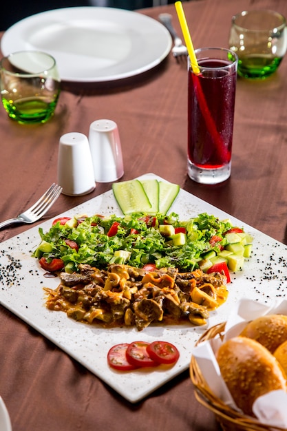 Vista lateral de carne frita com cogumelos em molho com salada de legumes e fatias de tomate e pepino